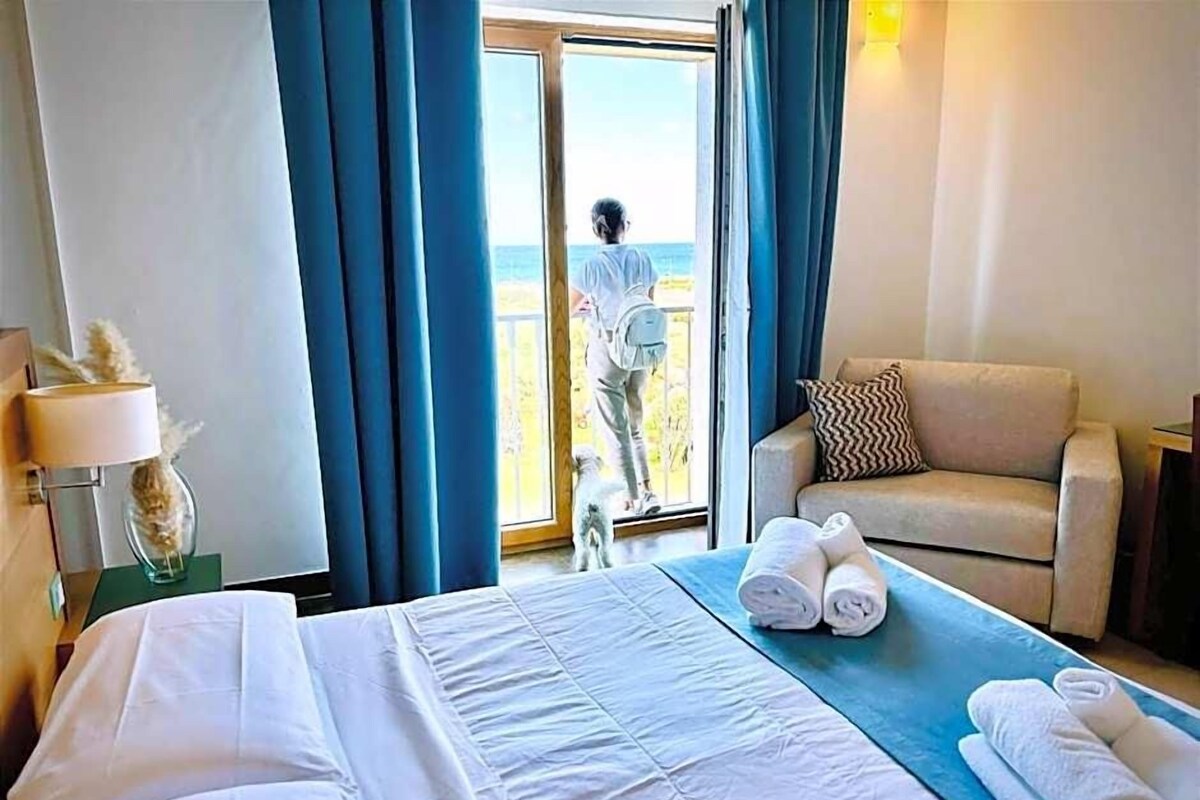 A hotel room with a bed, a sofa, a balcony, and a view of the sea.