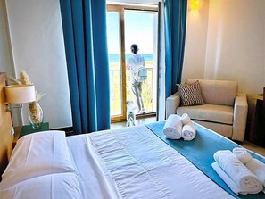 Quarto de hotel com cama, sofá, varanda e vista para o mar.