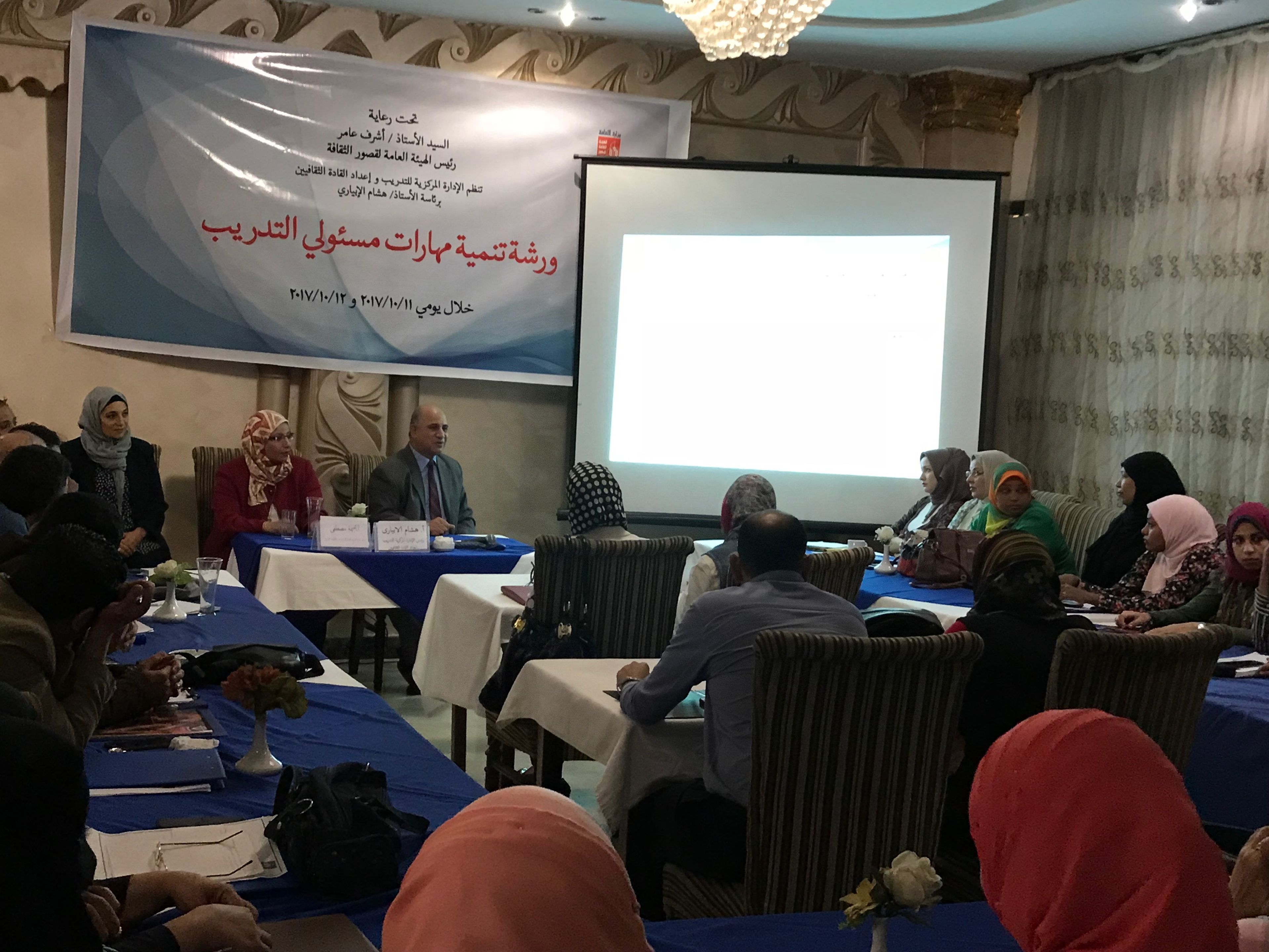 Une salle de conférence avec une banderole, des tables et des participants.