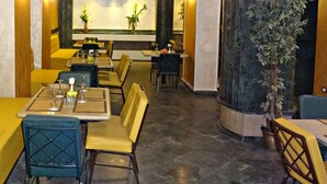 A restaurant interior with tables, chairs, a chandelier, and a large column with a plant. - Indiana Hotel Cairo (Giza)