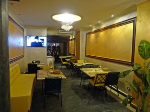 Interior de restaurante con mesas, sillas, una pantalla de televisión y una araña.