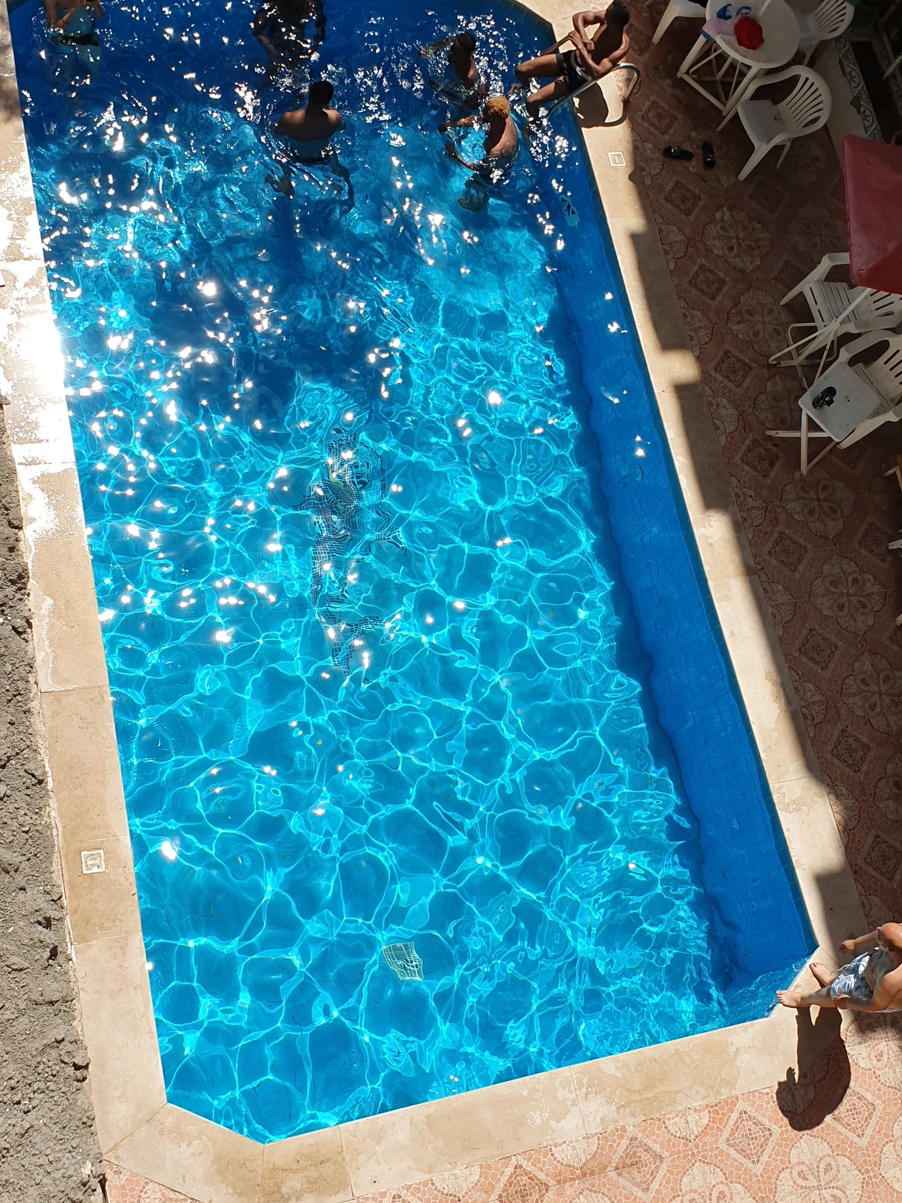A swimming pool with clear blue water, surrounded by tiled flooring and white plastic chairs.