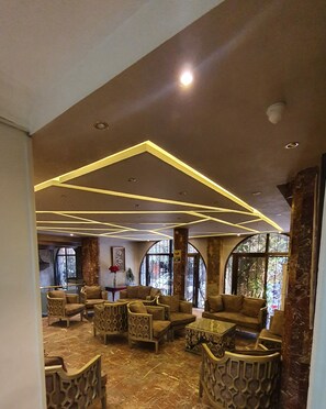 Un vestíbulo espacioso con mobiliario moderno, un techo alto con iluminación geométrica y grandes ventanales que dejan entrar luz natural.