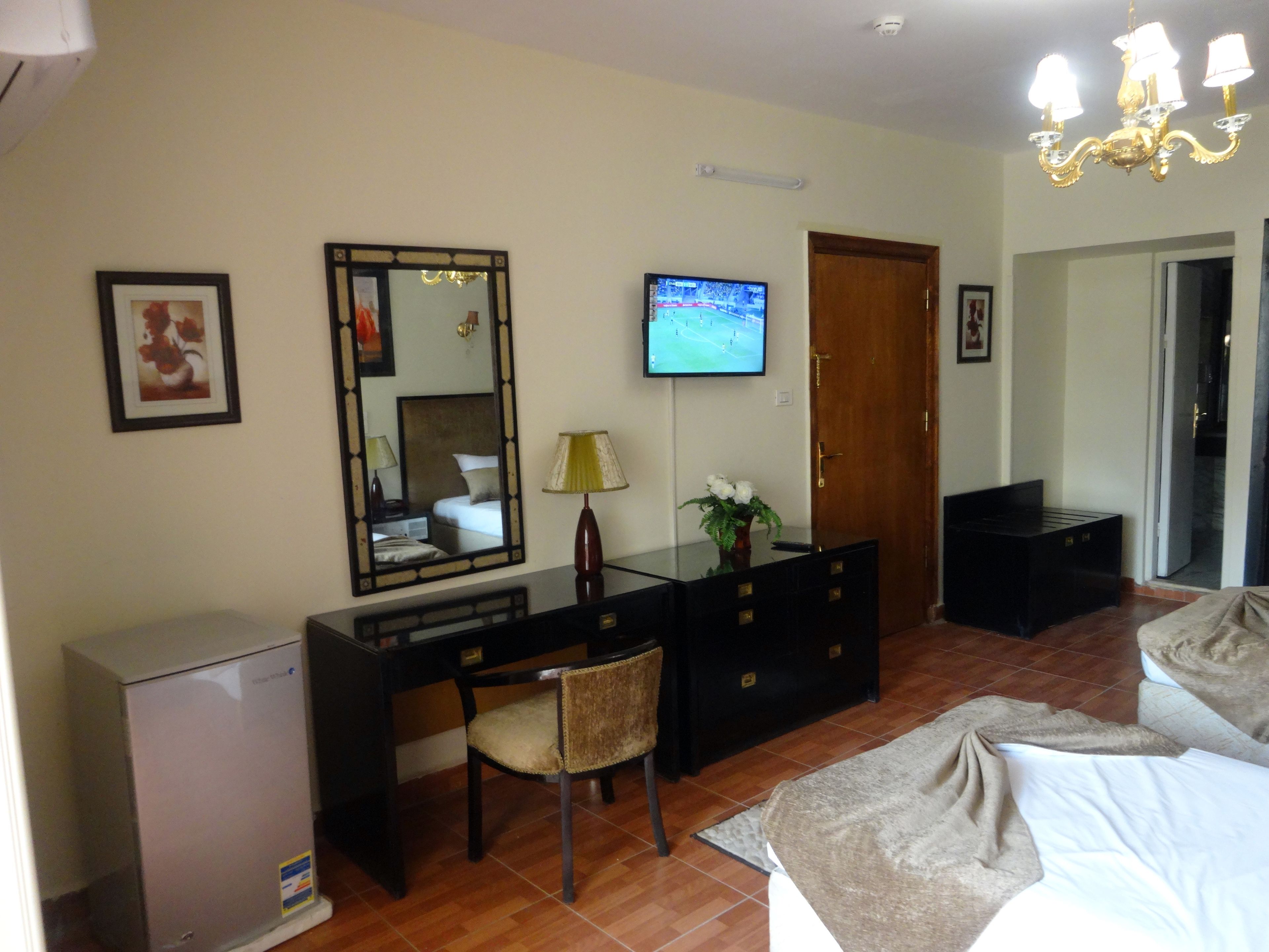 Une chambre d’hôtel équipée d’un lit, d’un bureau, d’une télévision, d’un miroir, d’une armoire et d’un petit réfrigérateur.
