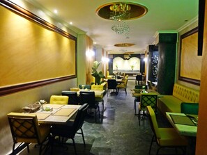 En restaurang med flera bord och stolar, en bardisk och en sittgrupp med bekväma bänkar.