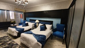 A hotel room with two beds, a blue armchair, a chandelier, and a window with curtains. - Indiana Hotel Cairo (Giza)