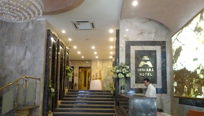 Vestíbulo de hotel con suelo de mármol, una recepción y una escalera que lleva a otra zona.