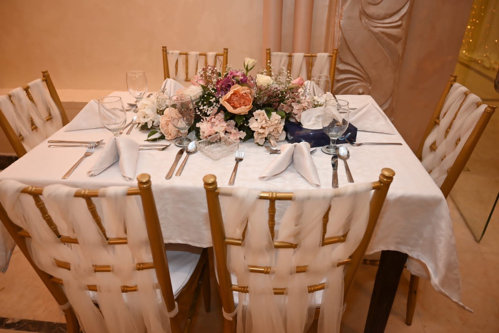 A round dining table with white tablecloth, gold chairs, and a floral centerpiece.