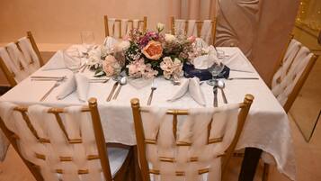 A round dining table with white tablecloth, gold chairs, and a floral centerpiece.