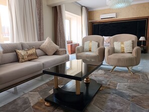 Una sala de estar moderna con un sofá, dos sillones, una mesa de centro de vidrio y un suelo con diseño de piedra.