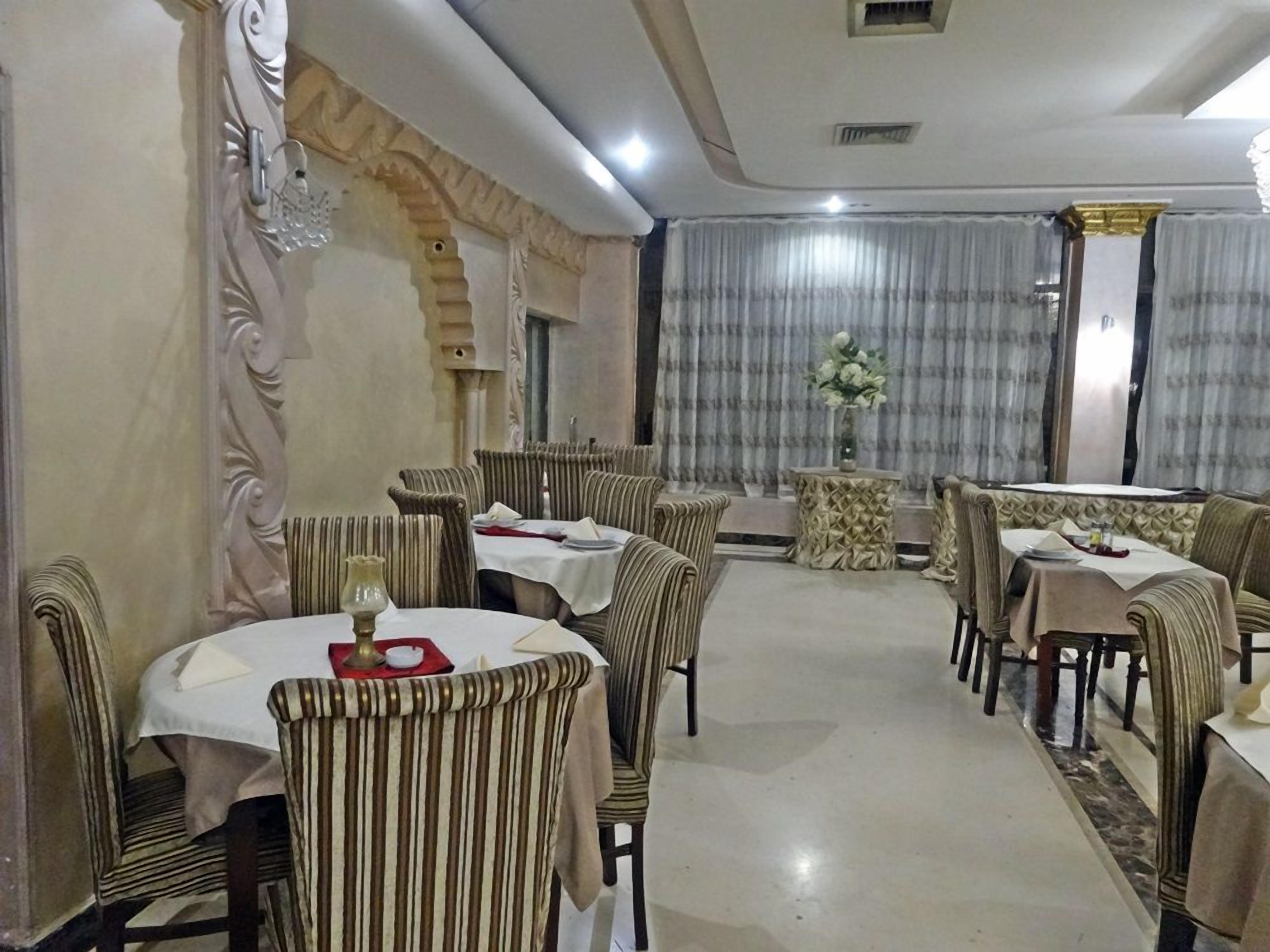 A dining area with round tables and striped chairs, a decorative wall, and a curtain with a floral arrangement.