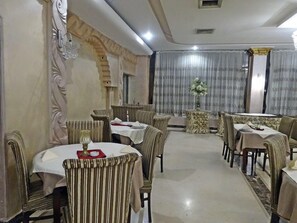 A dining area with round tables and striped chairs, a decorative wall, and a curtain with a floral arrangement.