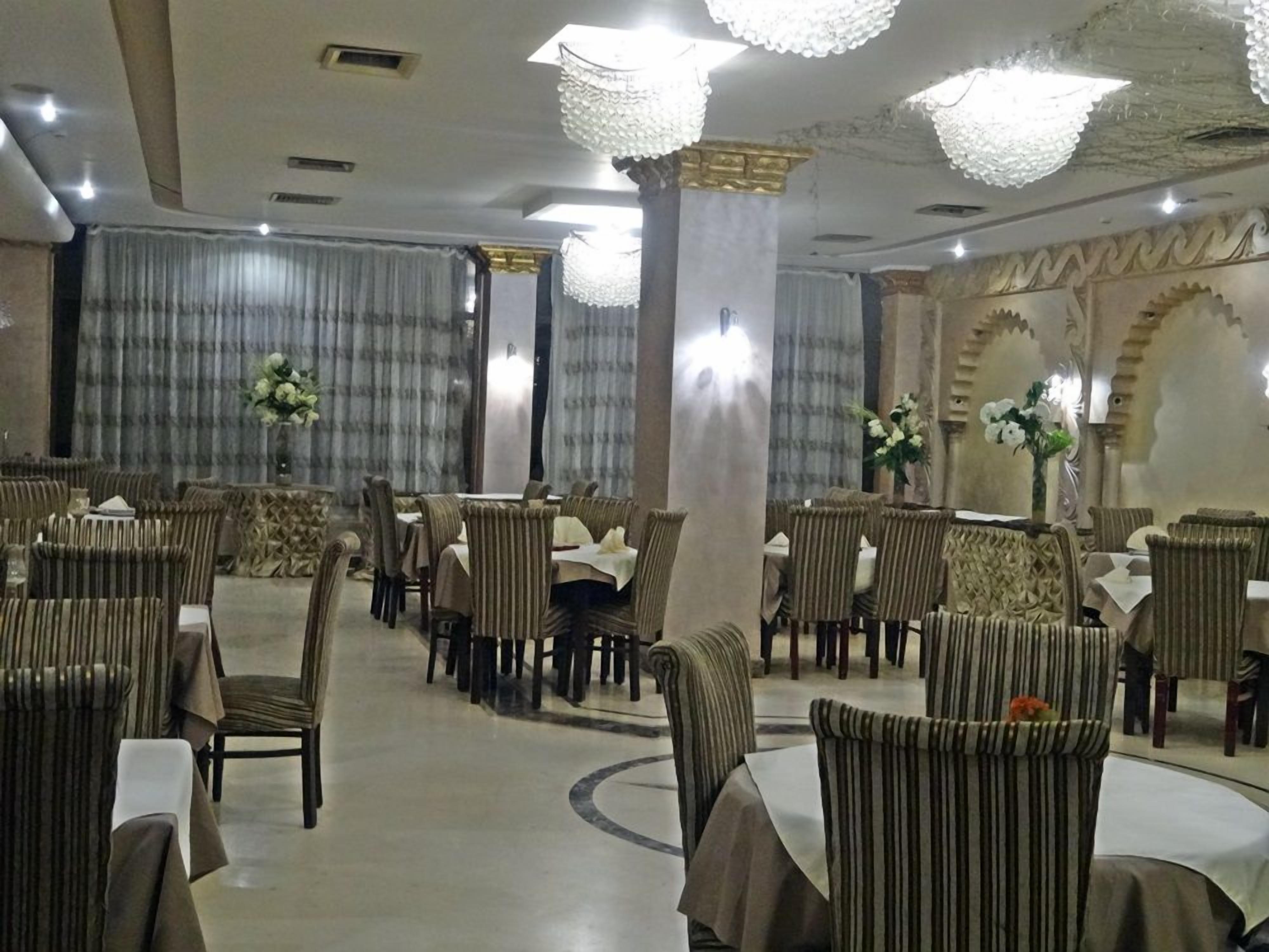 A banquet hall with round tables and chairs, chandeliers, and curtains.