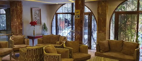 A lobby with a modern design, featuring a seating area with sofas and chairs, a marble coffee table, and large windows with a view of the outside.