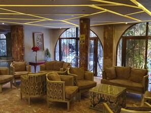 Eine Lobby mit modernem Design, inklusive einer Sitzecke mit Sofas und Sesseln, einem Marmortisch und großen Fenstern mit Ausblick.