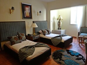 Una habitación de hotel con dos camas, una zona de estar, un ventanal y una lámpara.