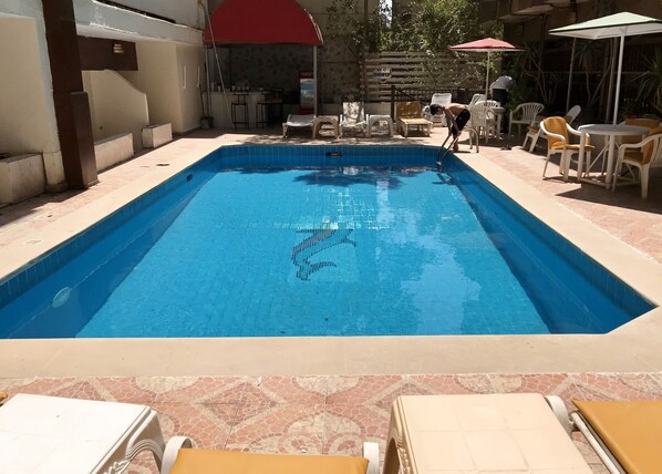 Piscina rectangular con bordes de azulejos, rodeada de sillas de descanso y sombrillas.