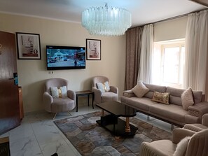 Ett vardagsrum med en soffa, två fåtöljer, ett soffbord, en tv och en kristallkrona.