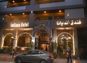 Das Außengelände des Indiana Hotels mit beleuchteter Beschilderung, bogenförmigen Eingängen und Pflanzgefäßen.