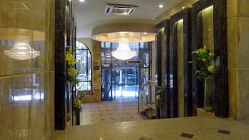 A hotel lobby with marble flooring, a grand chandelier, and a reception desk.