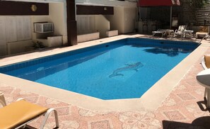Ein rechteckiger Swimmingpool mit einer gefliesten Kante, umgeben von Liegestühlen und einer gefliesten Liegefläche.