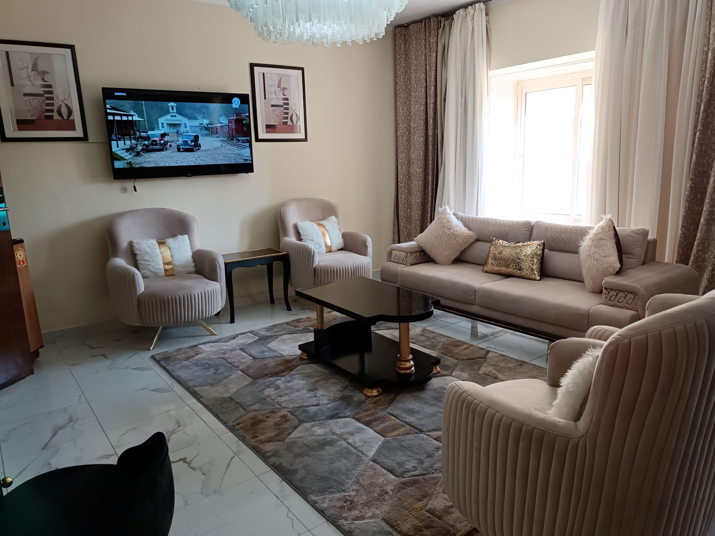 A living room with a sofa, two armchairs, a coffee table, and a TV mounted on the wall.
