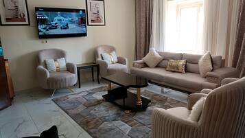 A living room with a sofa, two armchairs, a coffee table, and a TV mounted on the wall.