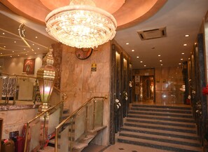 A hotel lobby with a grand chandelier, marble walls, a staircase, and a reception area.