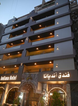 Ett hotell med flera våningar, balkonger och en skylt som visar texten ”Indiana Hotel” och ”Indiana Hotel” på arabiska.