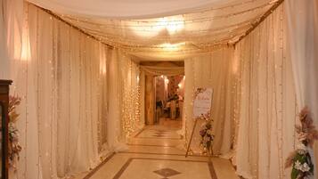 A corridor with draped fabric and string lights, leading to a reception area with a welcome sign.