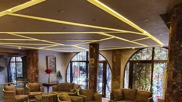 A lobby with a modern design, featuring a seating area with sofas and chairs, a coffee table, and a decorative ceiling with geometric lighting.