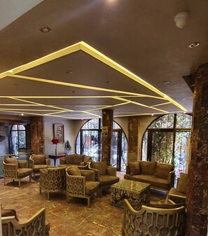 A lobby with a modern design, featuring a seating area with sofas and chairs, a coffee table, and a decorative ceiling with geometric lighting. - Indiana Hotel Cairo (Giza)