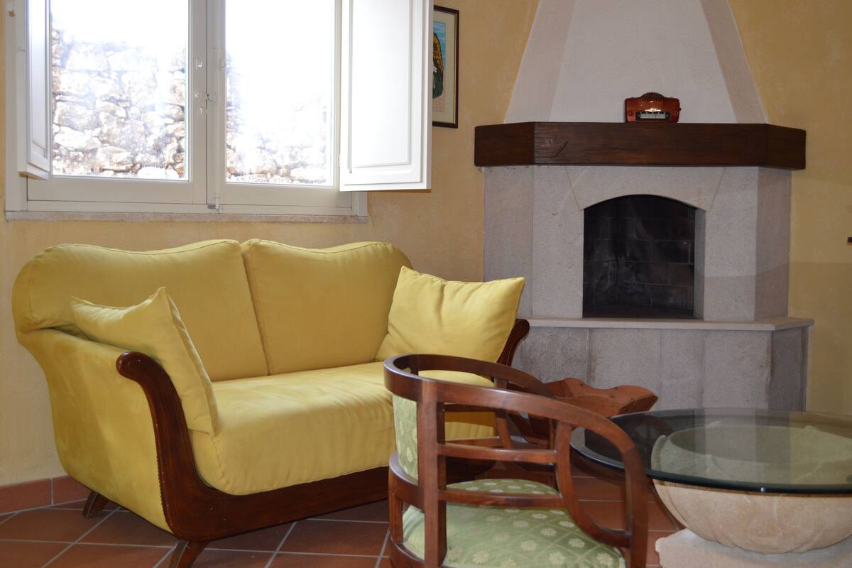A living room with a yellow sofa, a wooden chair, a glass-top table, and a fireplace.