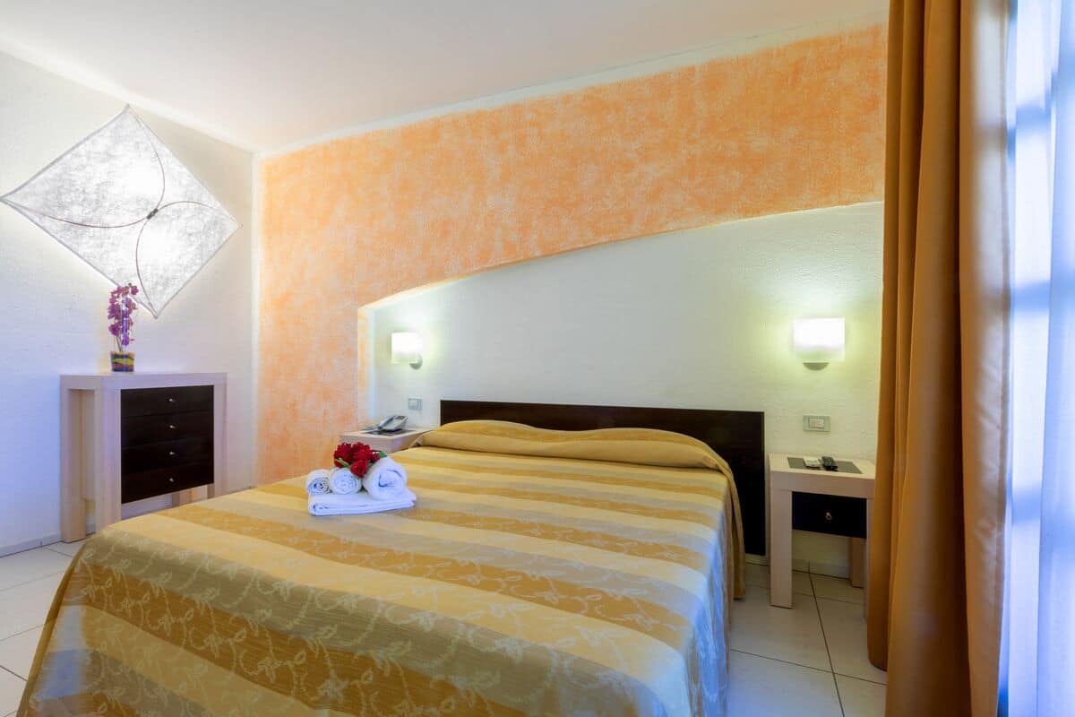 A hotel room with a large bed, a bedside table with a lamp, and a nightstand with a phone.