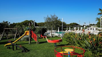 Relax by the pool surrounded by lush greenery and palm trees, with a children's play area nearby.