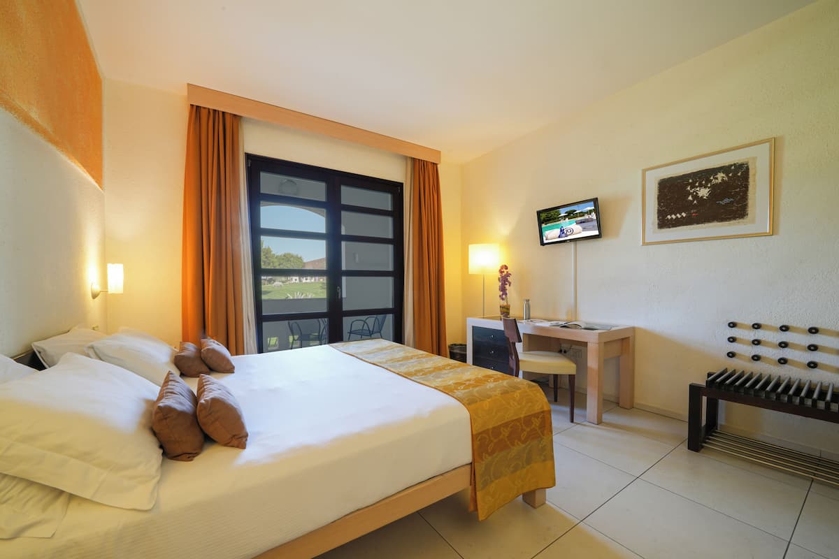 A hotel room with a bed, desk, chair, TV, and a view of the outdoors.