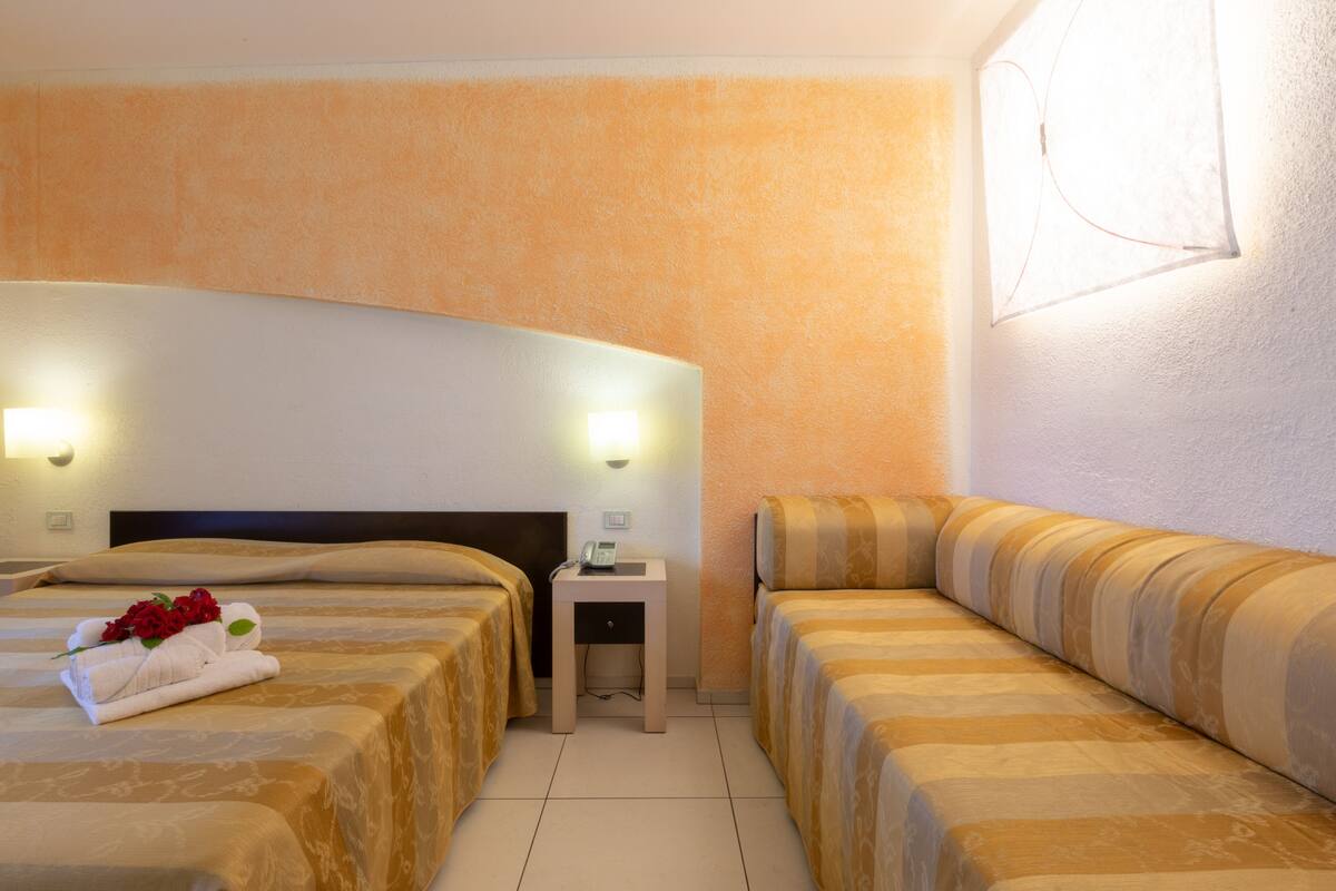 A hotel room with two beds, a nightstand, and a wall-mounted light fixture.