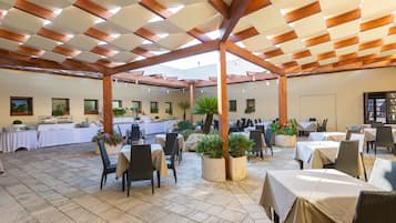 Un amplio espacio exterior con mesas y sillas, una estructura de pérgola y plantas en macetas.