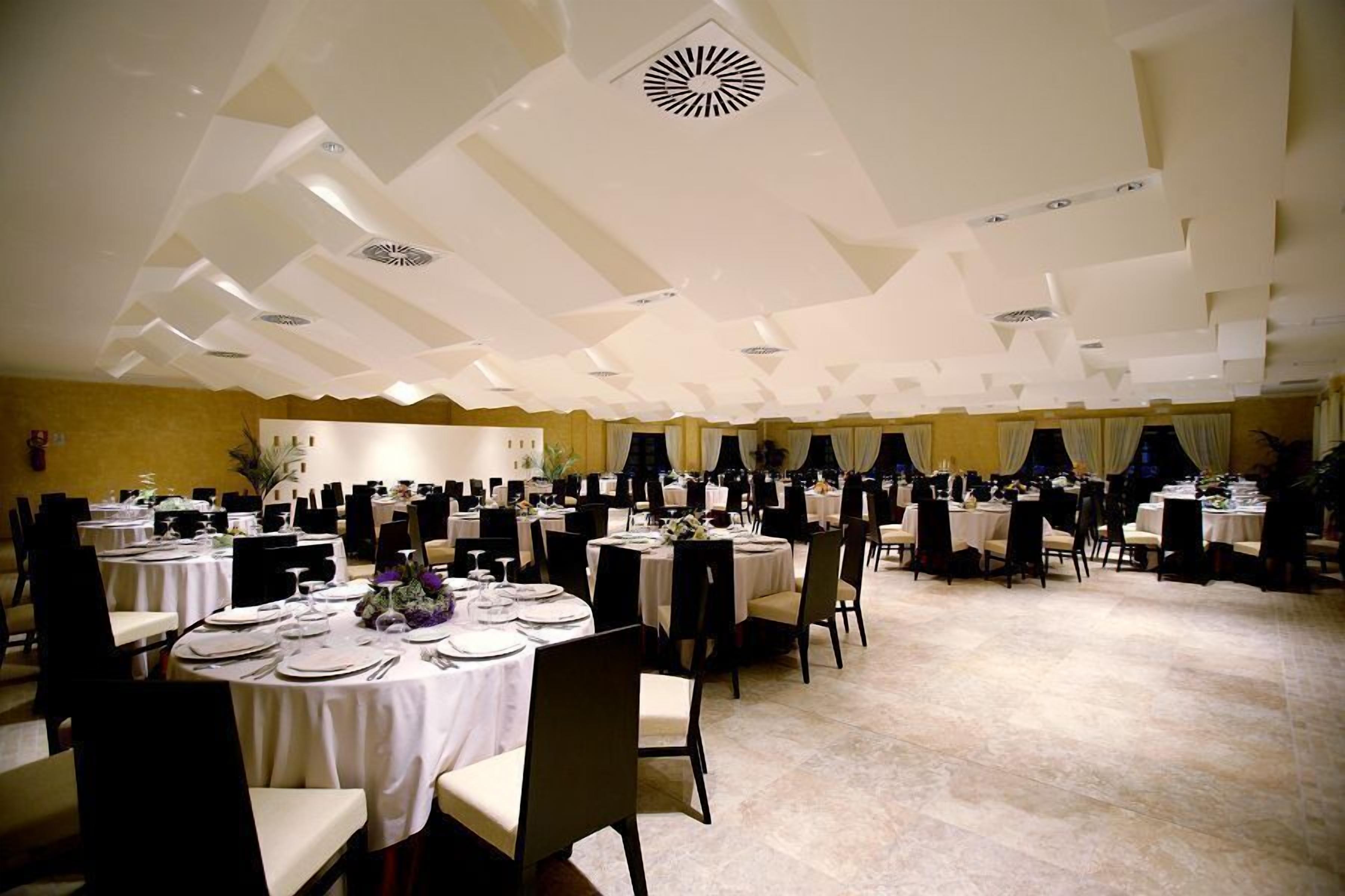 Un amplio salón de banquetes con mesas redondas dispuestas para cenar, con un diseño de techo moderno y abundante espacio para sentarse.