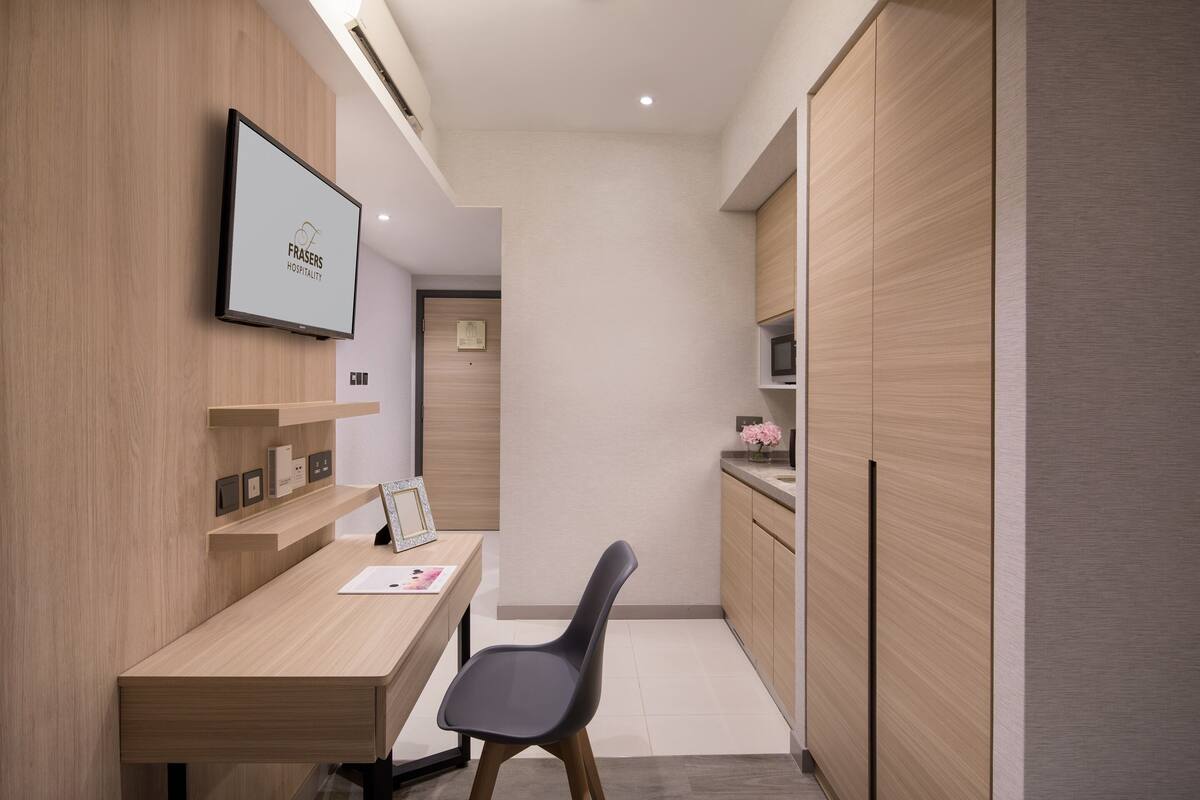 A modern hotel room with a wooden desk, a chair, a flat-screen TV, and built-in wooden cabinets.