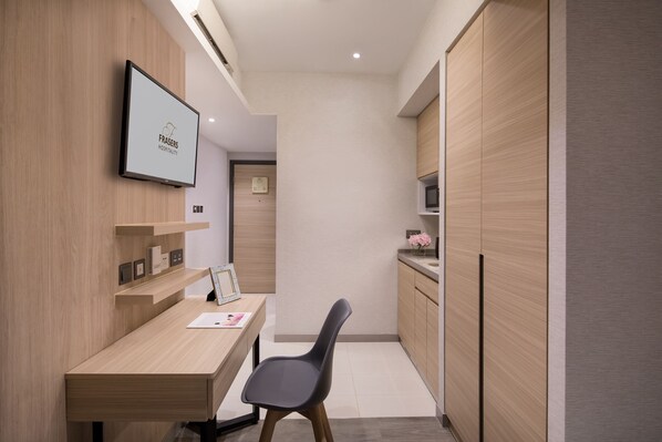 Une chambre d’hôtel moderne dotée d’un bureau en bois, d’une chaise, d’un téléviseur à écran plat et d’armoires encastrées en bois.