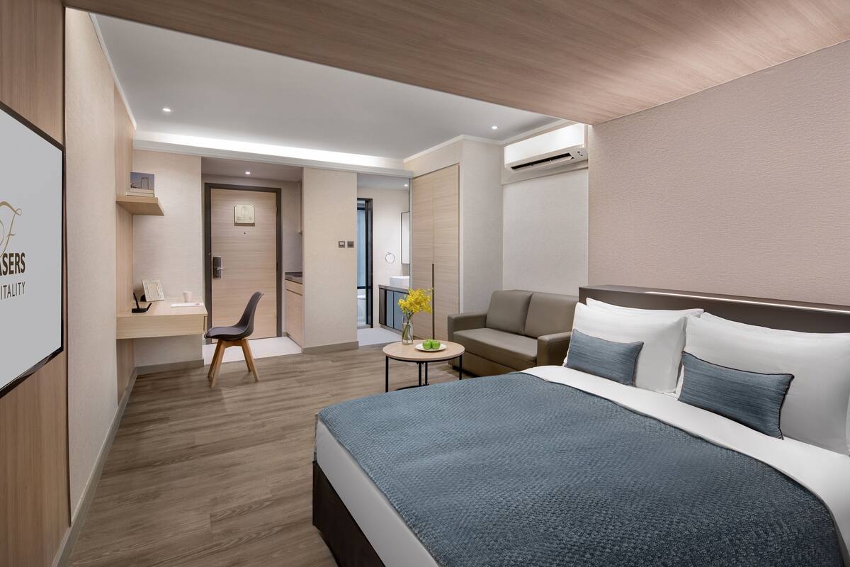 A modern hotel room with a large bed, a desk, a chair, and a small table with a vase of flowers.