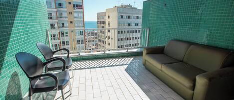 Ein Balkon mit grünen Fliesen, einem beigen Sofa und zwei schwarzen Stühlen.