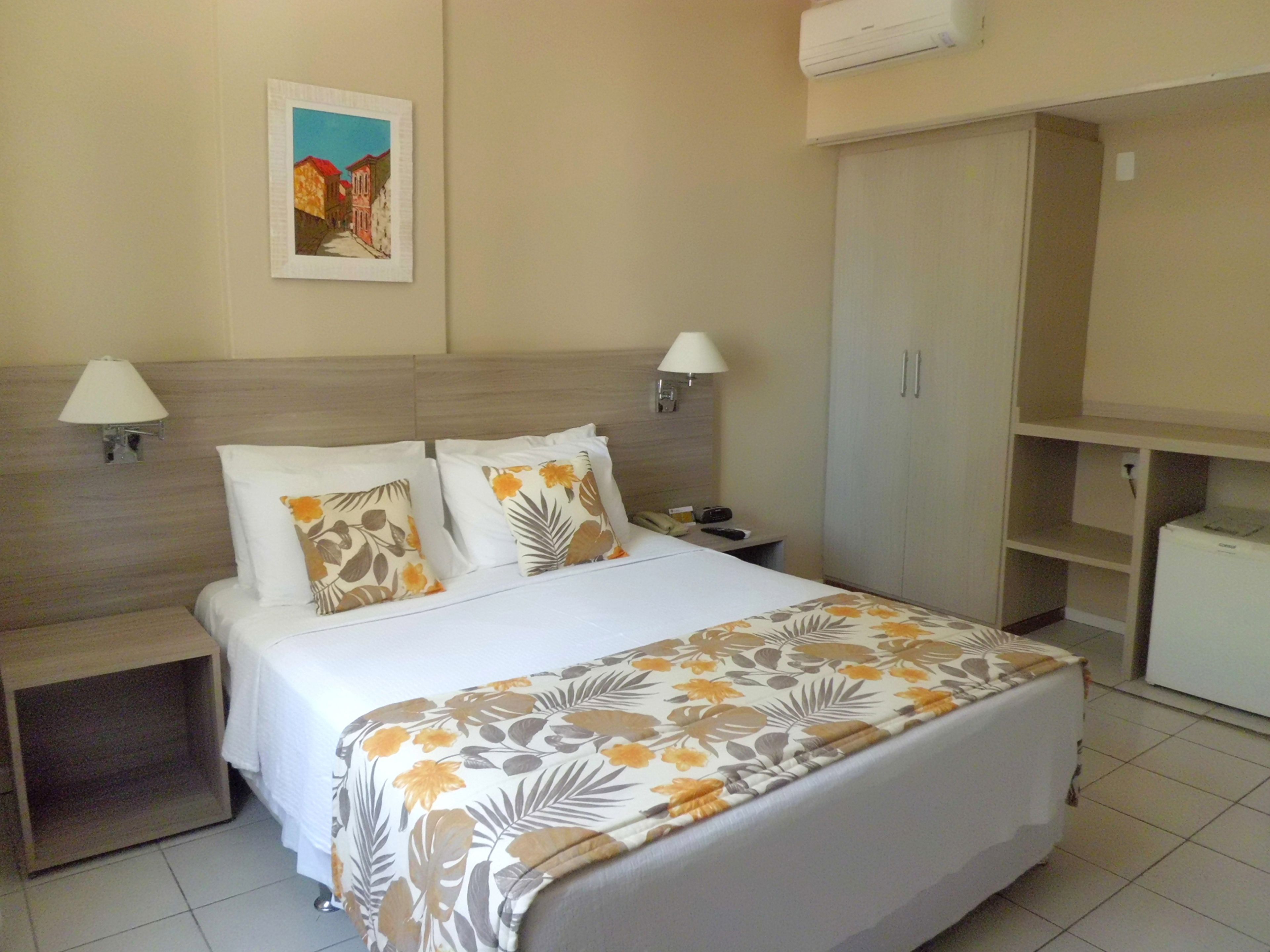 A hotel room with a bed, two bedside lamps, a nightstand, a wardrobe, and a painting on the wall.