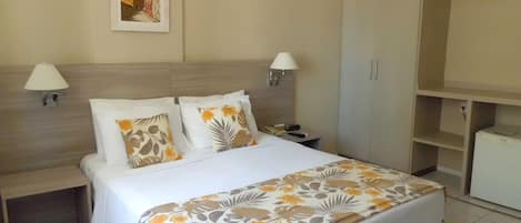 A hotel room with a bed, two bedside lamps, a nightstand, a wardrobe, and a painting on the wall.