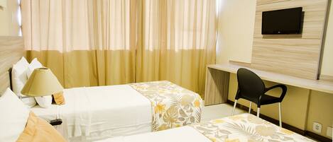 A hotel room with two beds, a desk, a chair, a TV, and a lamp.