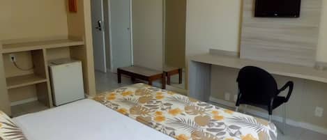 Habitación de hotel con cama, escritorio, silla, televisor y refrigerador pequeño.