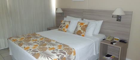 A hotel room with a large bed, two bedside tables, a nightstand, a lamp, a painting on the wall, and a window with curtains.