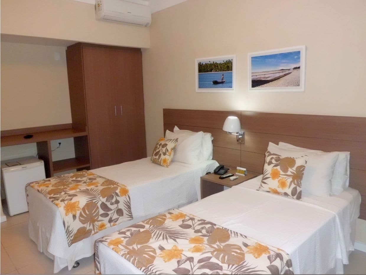Habitación de hotel con dos camas, un escritorio, un armario y dos cuadros en la pared.