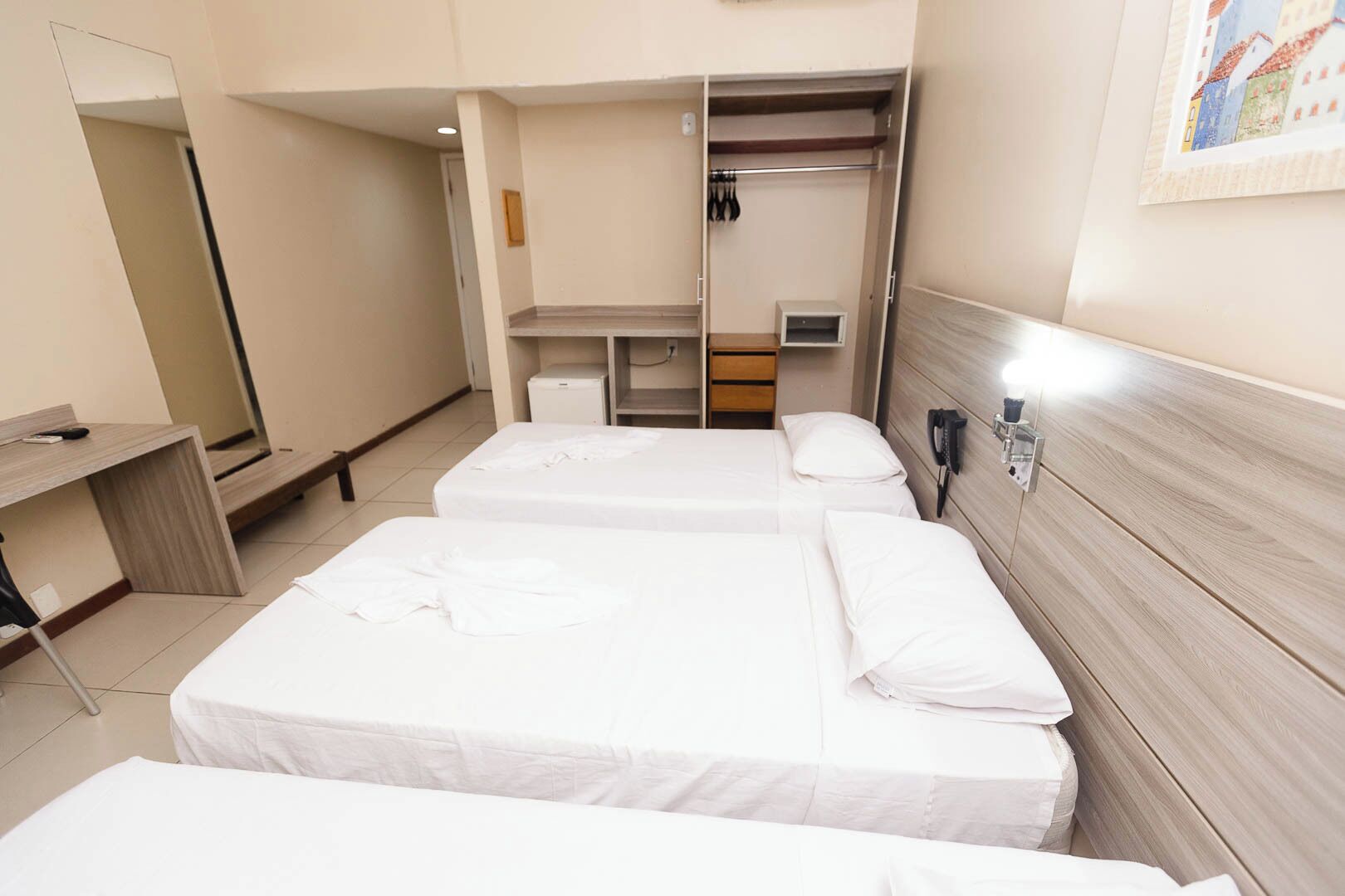 Een hotelkamer met drie eenpersoonsbedden, een bureau, een spiegel en een kledingkast.